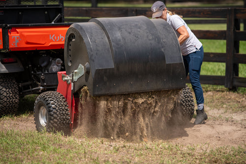 Person operating a Kubota tractor with a large black roller in a field