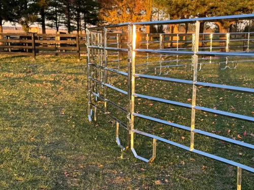 Row of galvanized livestock corral panels curving through a pasture with autumn trees in the background