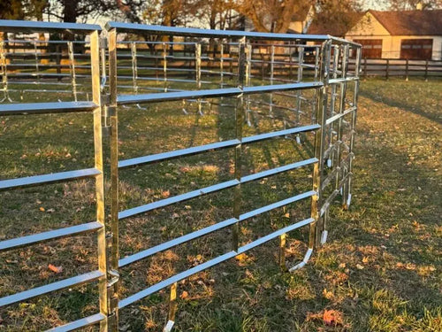 Row of galvanized livestock corral panels in a pasture with a farmhouse and barn in the background