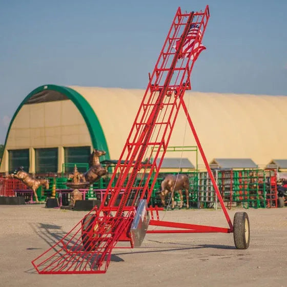 Red steel hay elevator on wheels parked outside a Quonset-style farm building