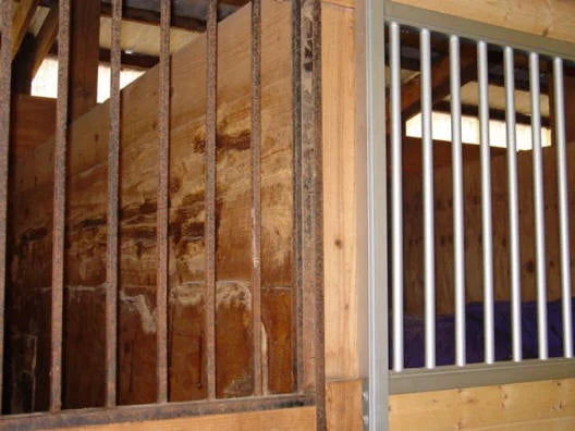 Side-by-side comparison of an old rusted steel horse stall next to a new galvanized stall installation